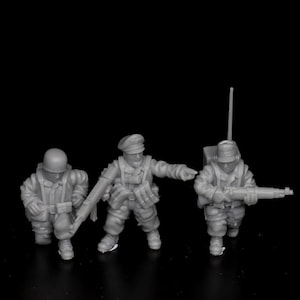Può includere: Tre soldatini di plastica grigi in uniforme militare, uno con un fucile, uno con una radio e uno inginocchiato con un fucile.