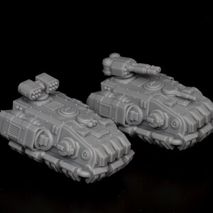 Op de afbeelding: Twee grijze miniatuurtanks met gedetailleerde ontwerpen, waaronder torentjes, raketwerpers en ingewikkelde panelen. De tanks staan tegen een zwarte achtergrond en tonen hun mechanische kenmerken en het algehele ontwerp.