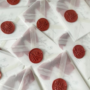 May include: A stack of white envelopes with red wax seals. Each seal has a leaf design. The envelopes are translucent and have a subtle sheen.