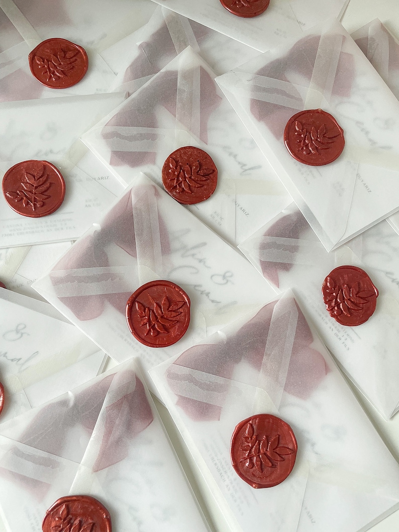 May include: A stack of white envelopes with red wax seals. Each seal has a leaf design. The envelopes are translucent and have a subtle sheen.