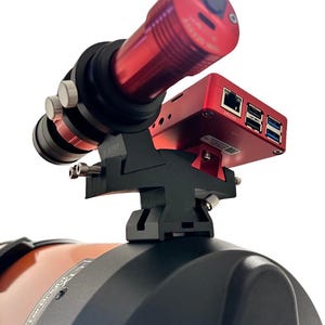 May include: A red and black telescope mount with a red camera and a black computer attached. The mount is attached to a black and orange telescope.