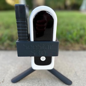 Può includere: Una telecamera di sicurezza SeeStar S30 bianca e nera con un treppiede nero.