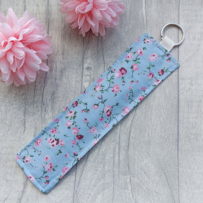 May include: A light blue key chain with a pink floral pattern. The key chain has a silver metal ring.