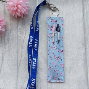 May include: A blue lanyard with the word "STAFF" repeated on it, attached to a small blue and white floral fabric pouch with two pens inside.