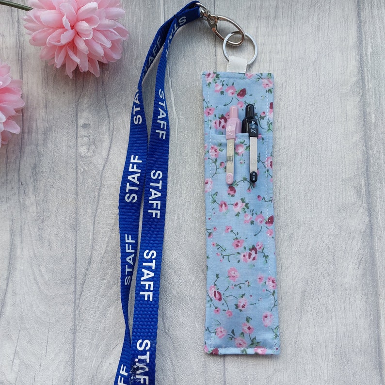 May include: A blue lanyard with the word "STAFF" repeated on it, attached to a small blue and white floral fabric pouch with two pens inside.