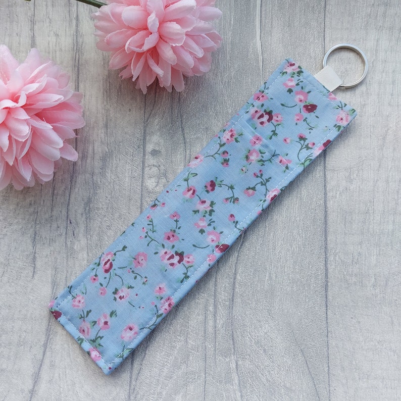May include: A light blue fabric key chain with a pink floral pattern and a silver key ring.