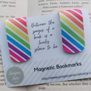 May include: Two rainbow striped magnetic bookmarks with the text "Between the pages of a book is a lovely place to be" and the website address "http://www.juniperjanecraft.etsy.com". The bookmarks are made by Juniper Jane Craft.