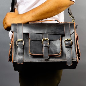 May include: A black leather satchel with brown leather accents and brass buckles. The bag has a large front pocket and a flap closure.
