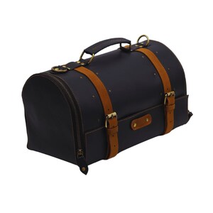 May include: Black leather duffel bag with tan suede straps and brass hardware. The bag has a rounded shape, a top handle, and a zipper closure. The bag is decorated with small brass rivets.