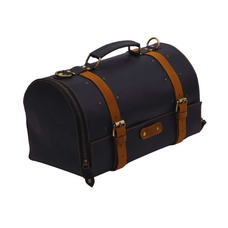 May include: Black leather duffel bag with tan suede straps and brass hardware. The bag has a rounded shape, a top handle, and a zipper closure. The bag is decorated with small brass rivets.