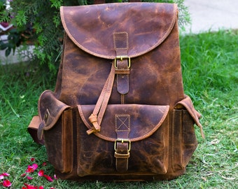 May include: A brown leather rucksack with a large front pocket and a buckle fastening. The rucksack has a distressed look and is made from high-quality leather.