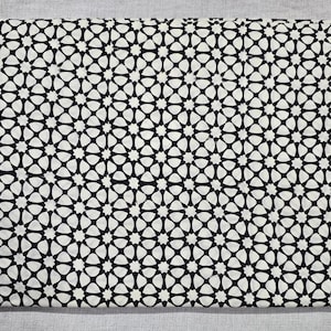 May include: Folded fabric with a repeating black and white geometric star pattern. The fabric is a neutral color, and the pattern is a bold, symmetrical design. This textile could be used for various sewing and crafting projects.