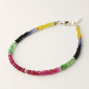 May include: A multi-colored gemstone bracelet with a silver clasp. The bracelet features red, green, blue, black, and yellow gemstones.