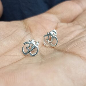 May include: A pair of silver Om symbol earrings. The earrings are small and delicate, and they are perfect for everyday wear.