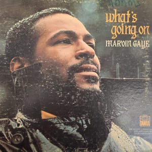 May include: Vintage vinyl record album cover featuring Marvin Gaye. The album title "What's Going On" is in gold lettering. Gaye's portrait is in the center, with a dark background. The album cover has a weathered appearance.