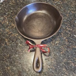 Może przedstawiać: Zestaw trzech ceramicznych kubków z nakrapianym, matowym wykończeniem. Kubki są w odcieniach kremu, jasnoszarym i ciemnoszarym. Każdy kubek ma prosty, minimalistyczny design i zaokrąglony uchwyt.