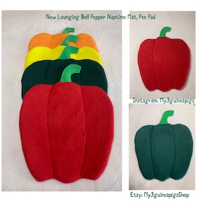 Pode incluir: Uma coleção de tapetes de sesta e resguardos em forma de pimento nas cores vermelho, verde escuro, amarelo e laranja. Cada tapete apresenta um caule verde e o texto New Lounging Bell Pepper Naptime Mat, Pee Pad, Instagram: My3guineapigs, Etsy: My3guineapigsShop.