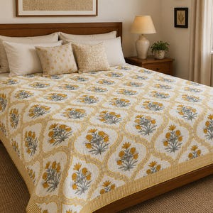 Könnte beinhalten: Eine Tagesdecke mit einem sich wiederholenden gelb-weißen Vierpass-Gittermuster und gelb-grauen Blumenmotiven. Der Quilt hat einen gelb gestreiften Rand und bedeckt ein Bett mit zwei cremefarbenen Kissen und zwei gemusterten Zierkissen.