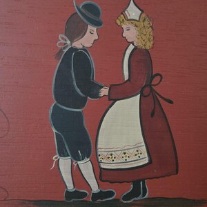 May include: A folk art painting on a red background depicts a couple in traditional attire holding hands. The man wears a black hat, jacket, and shorts. The woman is in a red dress with a white apron. The artwork has a simple, charming style.