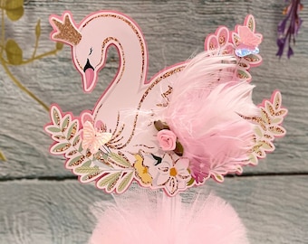 May include: Pink swan cake topper with gold glitter and floral accents. The topper is on a pink tulle base with a gold glitter band. The card below reads "Thank You for supporting my small business. Love it? Please snap it and share it or leave a review. Wood & crafts by jo. Custom deco for you. @woodandcraftsbyjo"