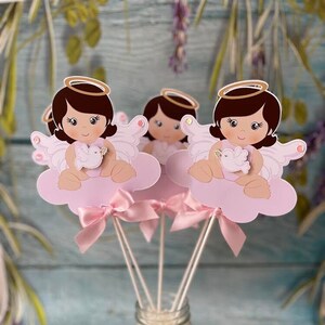 May include: Three pink and white angel baby centerpieces with gold halos and wings. Each angel is holding a white dove. The centerpieces are in a clear glass jar with white beads and a pink ribbon.