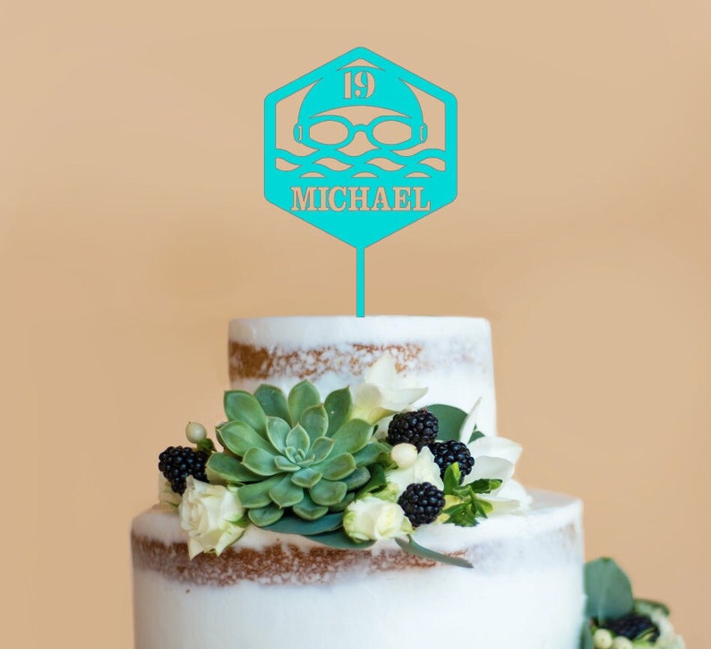 Peut inclure: Un topper de g&acirc;teau bleu turquoise avec un nageur portant un bonnet de bain et des lunettes de natation, le num&eacute;ro 19 et le nom "MICHAEL".