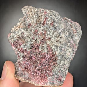 May include: A rough, irregularly shaped rock formation with a mix of gray and white crystalline structures. The rock features clusters of vibrant, deep red mineral deposits throughout its surface. The overall texture appears coarse and uneven.