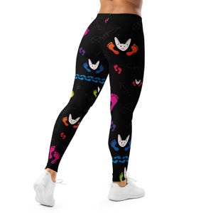 May include: Black leggings patterned with bunny faces, footprints, and doodles in various colours. The leggings have a high waist and a close fit. The design incorporates rainbow hues and a playful aesthetic.