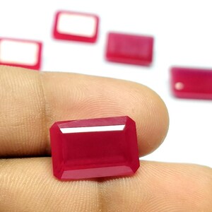 May include: A vibrant, rectangular, faceted red gemstone with a polished surface. The stone features sharp, clean edges and a deep crimson hue. Several additional identical red gemstones are arranged in the background, out of focus.