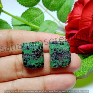 Peut inclure: Deux pierres précieuses rectangulaires en rubis zoïsite présentant une base vert vif avec des inclusions proéminentes de hornblende noire et des taches de rubis magenta foncé. Les pierres ont une surface lisse et polie.