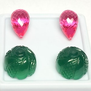 Puede incluir: Dos gemas rosas facetadas en forma de lágrima y dos gemas verdes talladas se muestran sobre una superficie blanca. Las piedras rosas tienen un corte brillante, mientras que las piedras verdes son redondas con un patrón detallado.