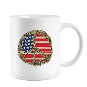 May include: White ceramic coffee mug with a peace sign design. The peace sign is filled with an American flag pattern and a leopard print border.