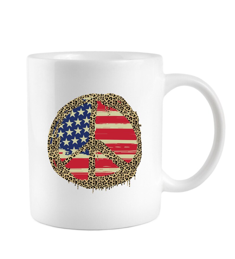 May include: White ceramic coffee mug with a peace sign design. The peace sign is filled with an American flag pattern and a leopard print border.