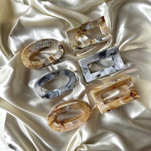 Peut inclure: Six pinces à cheveux de différentes formes ovales et rectangulaires avec un motif marbré dans des tons de brun, blanc et gris.