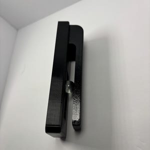 May include: A black, rectangular object with a curved handle. A small, clear, spherical object is visible between the two parts of the handle. The object is set against a white background.