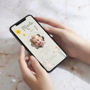 Puede incluir: Un tel&eacute;fono inteligente que muestra una invitaci&oacute;n de cumplea&ntilde;os para una ni&ntilde;a llamada Marla que cumple un a&ntilde;o. La invitaci&oacute;n presenta una foto de la ni&ntilde;a, un dise&ntilde;o floral y el texto "Marla wird 1" y "Du bist herzlich eingeladen".