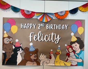 May include: A brown banner with the text "HAPPY 2ND BIRTHDAY Felicity" and illustrations of cartoon animals and balloons. A colorful paper fan garland hangs above the banner. The banner is displayed on a white door.