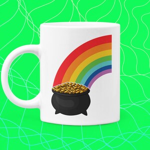 Può includere: Una tazza in ceramica bianca con un arcobaleno e un pentolone d'oro alla fine dell'arcobaleno. Il pentolone d'oro è nero con un bordo dorato ed è pieno di monete d'oro.