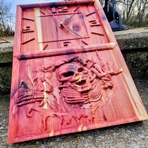 May include: A rectangular wooden clock with a carved design. The clock face has Roman numerals and ornate hands. Below the clock face is a carved image of a skeleton. The wood has a reddish-brown hue.