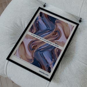 May include: A framed art print with abstract artwork in shades of blue, brown, and white, resting on a white upholstered chair. The print has the text "IF YOU WANT ME, IF YOU NEED ME, I'M YOURS" and the word "INNERBLOOM".