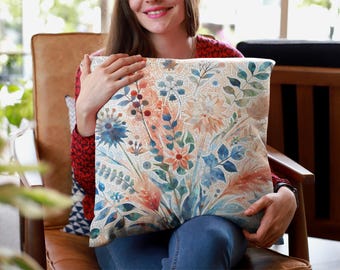 May include: A square throw pillow featuring a watercolor-style botanical print with various flowers, leaves, and stems in shades of orange, blue, teal, and cream. The design displays a mosaic-like texture across the surface of the fabric.