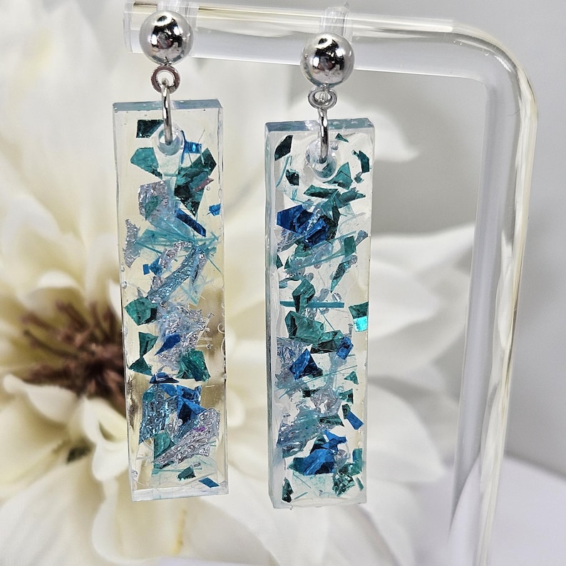 Op de afbeelding: Een paar zilveren oorhangers met rechthoekige blauwe en zilveren glitterharsstukken.