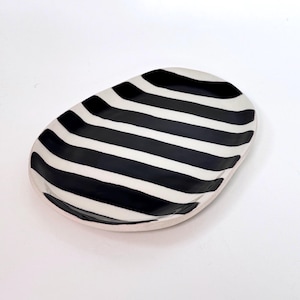 Könnte beinhalten: Eine weiße Keramik-Tasse mit schwarzem Henkel und dem Text "But First, Coffee" in schwarzer, handschriftlicher Schrift. Die Tasse steht auf einer weißen Oberfläche.