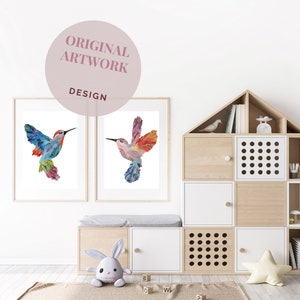 May include: Two framed prints of colorful hummingbird illustrations, one with a blue and green hummingbird and the other with a red and orange hummingbird. The prints are hanging on a white wall above a wooden bench with a white cushion.
