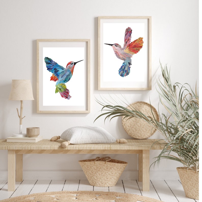 May include: Two framed prints of colorful hummingbird illustrations, one with a blue and green hummingbird and the other with a pink and red hummingbird, hanging on a white wall above a wooden bench with a white pillow, a woven basket, and a potted plant.