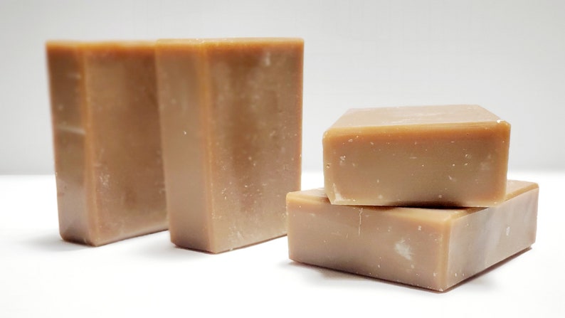 May include: Four bars of brown soap, stacked in a pyramid shape. The soap is a light brown color and has a slightly rough texture.