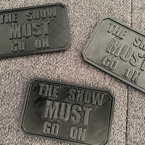 Peut inclure: Trois plaques rectangulaires noires avec le texte "The Show Must Go On" imprimé en blanc.