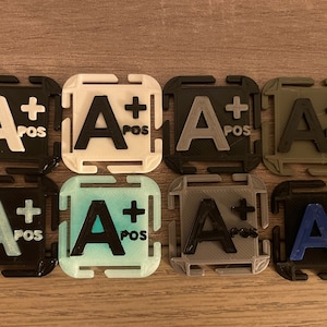 May include: Eight square-shaped plastic badges with the text "A+ POS" printed in black. The badges are in different colors: black, white, gray, green, blue, light blue, and two shades of teal.