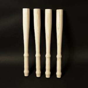 Könnte beinhalten: Vier unbehandelte Holztischbeine, jedes mit einer abgerundeten Oberseite und einem leicht konischen Boden.