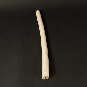 Peut inclure: Une baguette en bois naturel avec une légère courbure. La baguette est brute et a une surface lisse. L'extrémité de la baguette est fendue en deux.